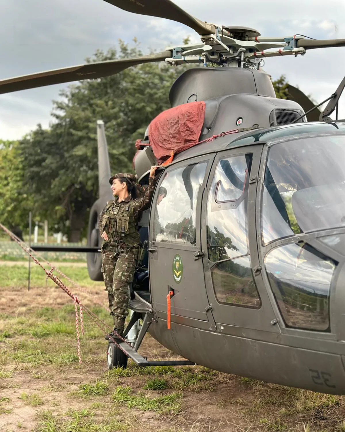 Suellen Bandeira de farda do Exército ao lado de um helicóptero